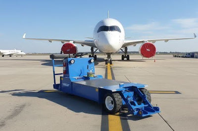 Blue aircraft tow tractor positioned in front of a commercial jet on an airport tarmac.